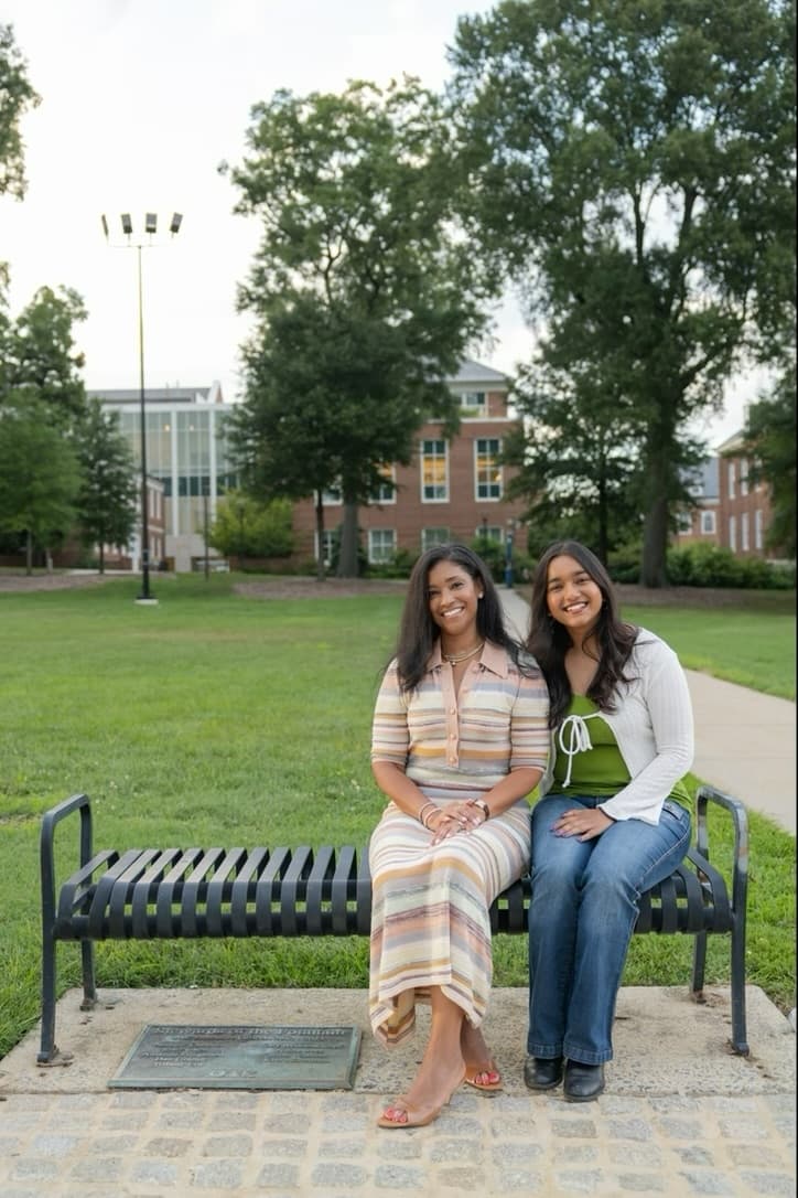 Ashley and Avishi sitting together on the same bench, laughing.